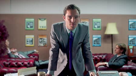 A sharply dressed salesman leans forward over a desk, exuding confidence and persuasion. Behind him, other salesmen lounge in a retro-styled office with framed product displays on the walls.